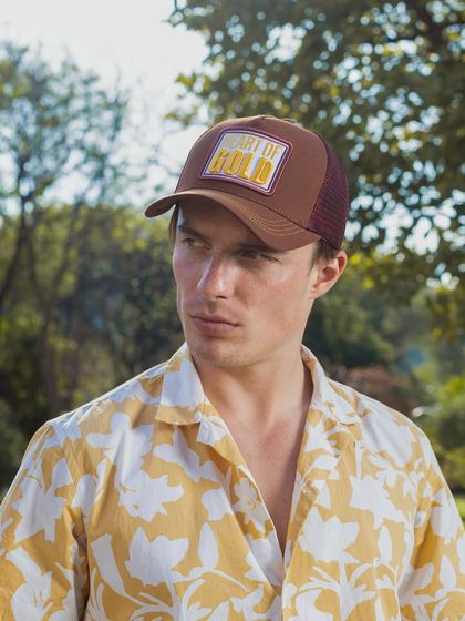 An outdoor lifestyle shot for a cap brand. The natural lighting and green background give the product a fresh, summery feel, showing how it can be styled for a day out.