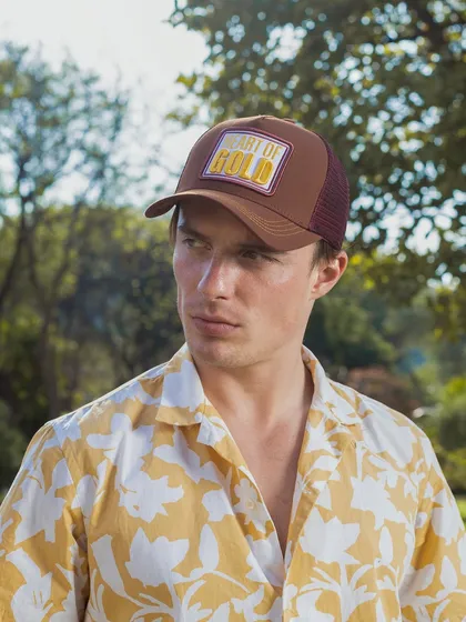 An outdoor lifestyle shot for a cap brand. The natural lighting and green background give the product a fresh, summery feel, showing how it can be styled for a day out.