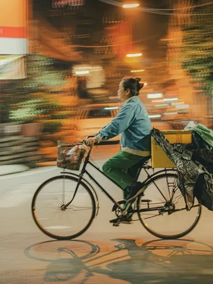 A street photograph from Hanoi using motion blur to capture a woman cycling, with a large bundle tied to the back of her bike.