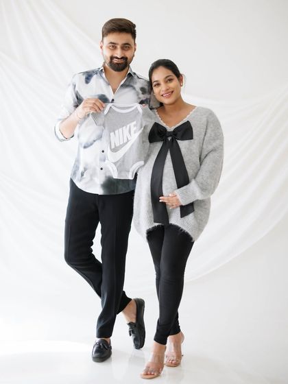 A classic family portrait pose, showing the couple's excitement by holding up a tiny baby outfit. It’s a sweet announcement and a cherished memory.