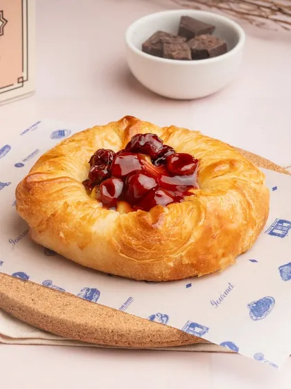 A vibrant seasonal fruit danish, topped with a glossy cherry filling that contrasts beautifully with the golden pastry.