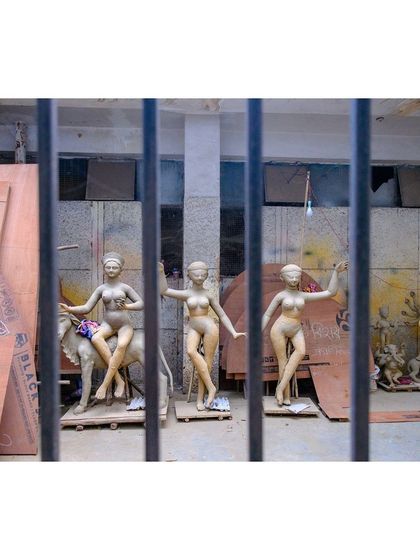 Unfinished clay idols seen through the bars of a workshop window, giving a glimpse into the world of the artisans.