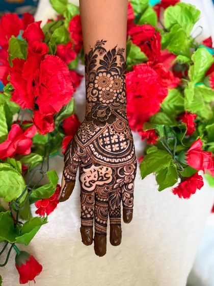 This beautiful semi bridal design features the name 'Azmi' in Arabic script, surrounded by a mix of floral and geometric patterns. The red flowers in the background make the henna pop.