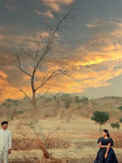 A dramatic wide shot of a couple in a vast, open landscape under a stunning sunset sky, perfect for a cinematic pre-wedding theme.