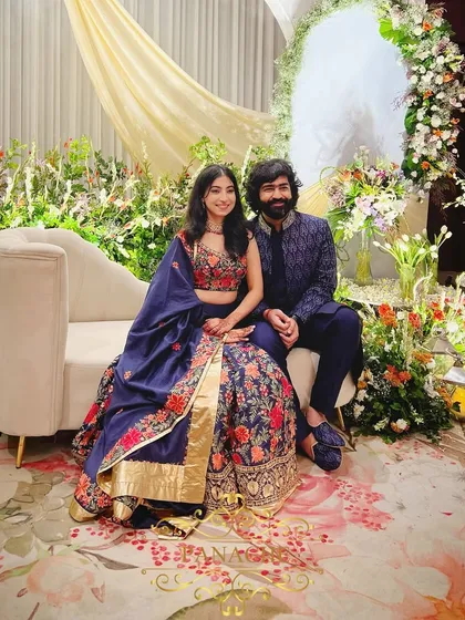 The couple seated on the elegant chaise lounge on their stage, surrounded by a garden of fresh flowers.