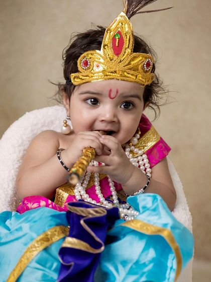A playful baby Krishna, with a bit of 'butter' on his face, sitting in a chair. His happy expression is what these shoots are all about.