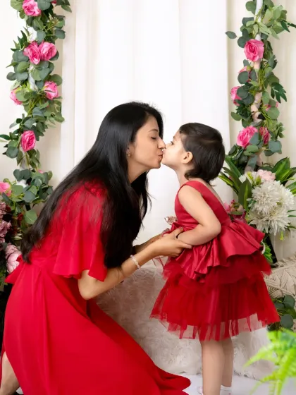 A sweet kiss between a mother and her daughter, both dressed in red, captured in front of our beautiful floral arch.