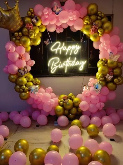 A princess-themed birthday decoration for an older child or teen. This setup features a pink and gold balloon ring, a royal crown prop, butterfly accents, and a central neon sign, creating a beautiful and celebratory photo spot.