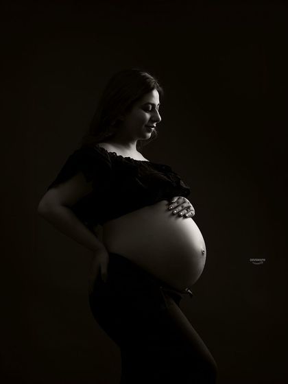 A classic low-key bare-bump profile shot. This style uses dramatic shadows to create a powerful and intimate portrait, focusing on the beautiful curves of pregnancy.