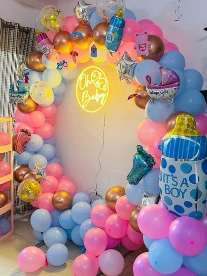 A very full and festive 'Oh Baby' balloon arch. This setup is packed with balloons in different sizes and colors, along with plenty of themed foils like baby bottles and footprints, creating a vibrant photo corner.