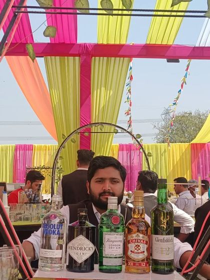 Our bartender ready to serve at a daytime Holi celebration, with a colorful canopy and a full selection of premium spirits.