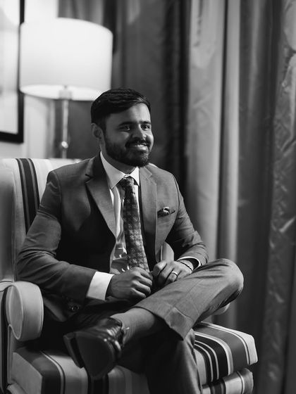 A candid black and white portrait of a groom, smiling during a quiet moment.