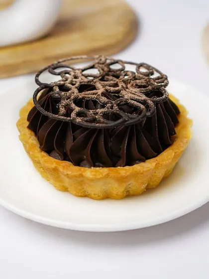 A beautifully crafted chocolate tart with piped frosting and a dusting of cocoa powder. The clean, bright composition makes this dessert look like a work of art.