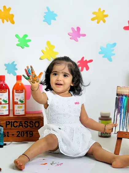 This little artist is proud of her work. The colorful paint splatters on the background add to the fun and creative energy of the shoot.