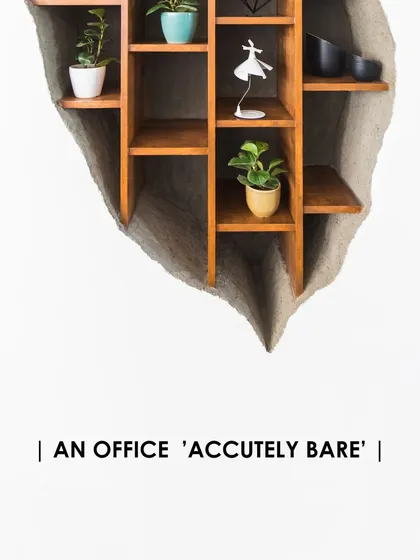 A custom-designed shelving unit appears to be carved out of the wall in the 'Acutely Bare' office. This detail combines raw texture with refined woodworking.