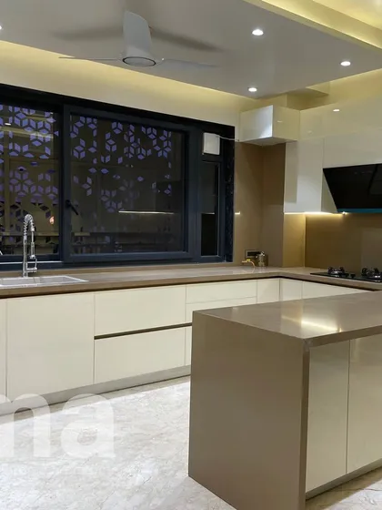 My design philosophy extends from the exterior to the interiors. This open-plan kitchen features a clean, handleless design with a calm, neutral palette. The large window, fitted with a custom jali screen, connects the interior space to the building's external architectural language, ensuring a cohesive feel throughout the home.