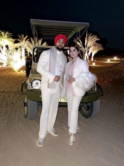 A client and his partner looking stunning in coordinated all-white outfits from us during a desert safari. His look features a custom white suit with a stylish scarf.