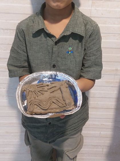 A student holding a clay relief sculpture he made. This technique involves creating a raised design on a flat surface, a great next step in pottery.