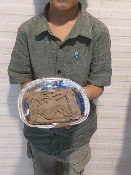 A child displays his clay relief sculpture. This activity teaches the basics of sculpting and allows for creative expression through a three-dimensional medium.