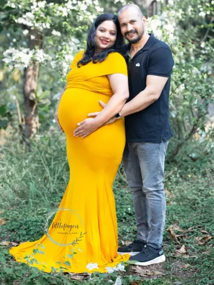 A radiant mother-to-be in a bright yellow gown, embraced by her partner. The natural, leafy backdrop makes the colors pop in this beautiful maternity portrait.