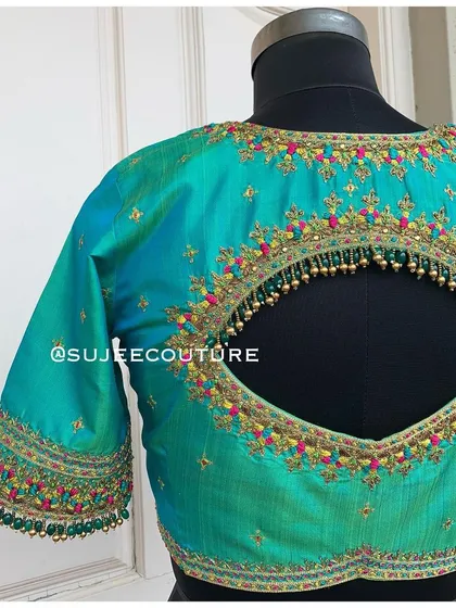 A vibrant teal blouse with a keyhole back design. The cutout is lined with colorful embroidery and delicate gold bead tassels, adding movement and charm.