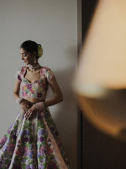A portrait of the bride in her unique floral lehenga, captured with a soft, dreamy focus. The out-of-focus lamp in the foreground adds an artistic layer to this beautiful shot.