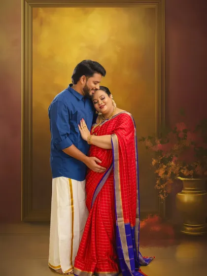 A beautiful South Indian couple's portrait, framed to look like a classic painting. The husband's traditional veshti and the wife's vibrant red saree create a culturally rich and intimate image.