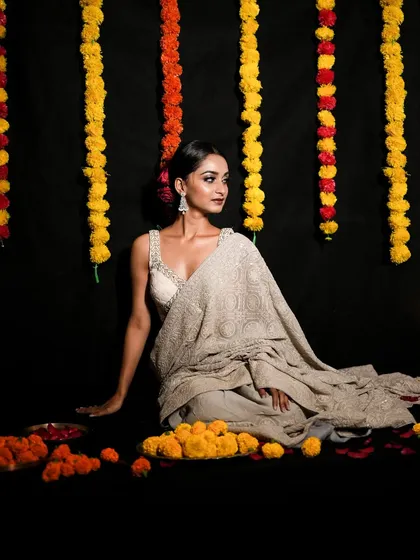 A festive Diwali portrait. The model is seated gracefully amidst marigold flowers, with traditional garlands hanging against a dark backdrop, creating a rich, celebratory mood.