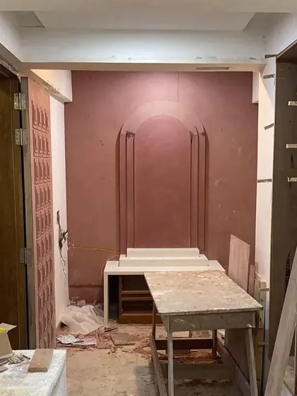A work-in-progress shot of the mandir space at Vishu Home. This shows the raw construction and application of the textured wall finish before the final elements are installed.
