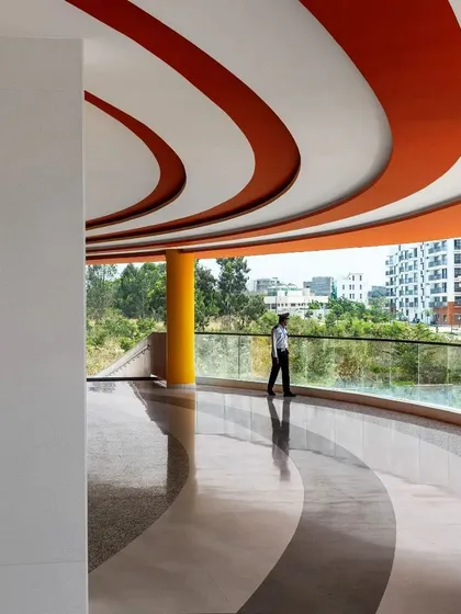 The interplay of curved forms on the ceiling and floor at the MARC Auditorium creates a sense of fluid movement. The open balcony provides a vantage point overlooking the campus, reinforcing the connection to the outdoors.