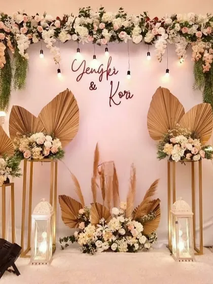 A boho-chic decor setup for a home celebration, using dried palm leaves, pampas grass, and a personalized name sign.