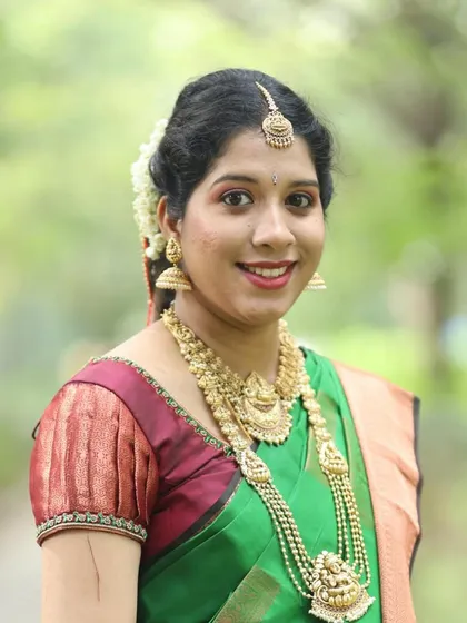 A smiling portrait of Dr. Shree Raksha. The layered temple necklaces add a touch of grace to her simple and beautiful look.