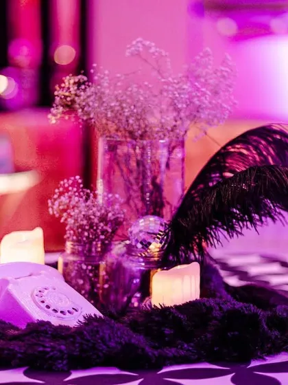 A retro-themed centerpiece for the Sangeet, featuring a vintage telephone, black feathers, and baby's breath, all bathed in dramatic purple light.