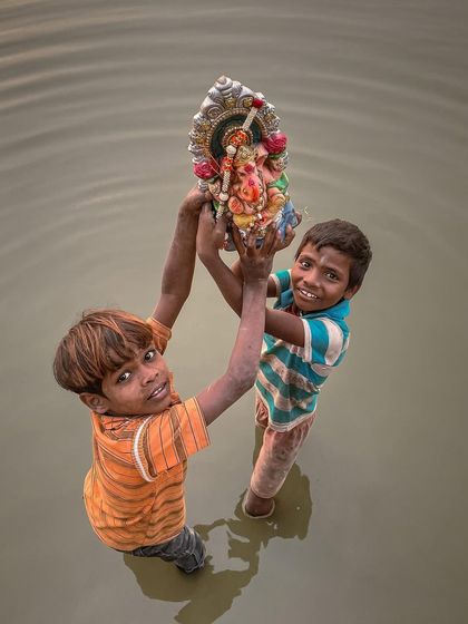 Two young boys rescue a Ganesha idol from the water after the immersion ceremony, their faces a mixture of effort and reverence.