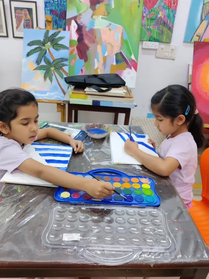 Two young sisters sit side-by-side, focused on their watercolor paintings. Art is a wonderful activity for siblings to share.