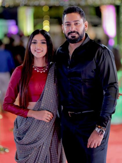 A posed shot of the Devaraj couple, showcasing their coordinated and fashionable outfits.