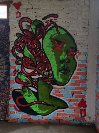 A piece I painted on a brick wall during a trip to Pulga. This mural, featuring a stylized green face with red floral elements, shows how I can adapt my art to different surfaces and environments, like this rustic interior space.
