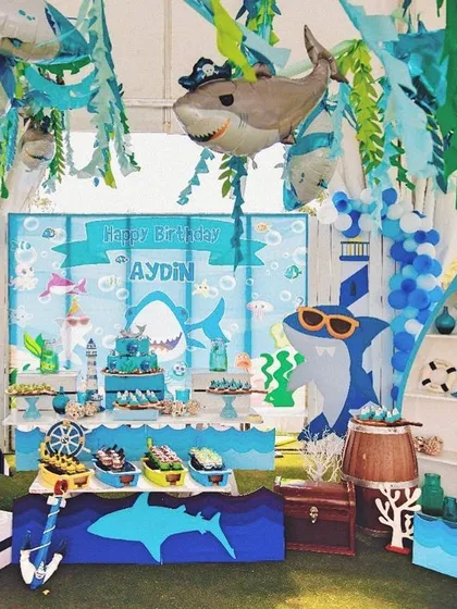 A "fin-tastic" Baby Shark birthday party. The entire setup was designed to feel like an underwater adventure, with shark cutouts, blue decor, and a boat-shaped shelf.
