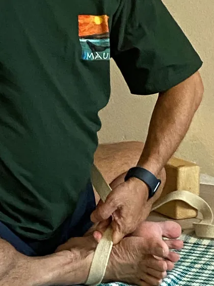 A close-up showing the precise way to wrap a strap around the feet for a seated pose. Correct prop usage is fundamental to the Iyengar method.