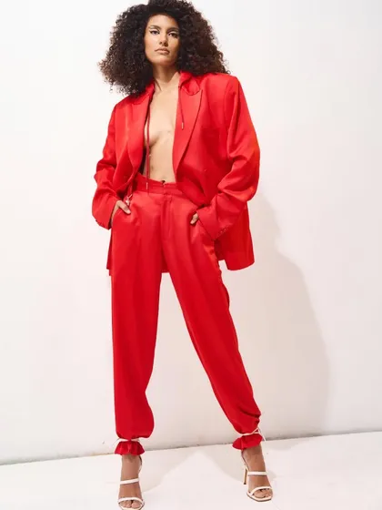A powerful statement in red. This full-body shot of a vibrant red satin pantsuit showcases a modern, bold aesthetic. The styling, with an open blazer and confident pose, is designed to convey strength and contemporary elegance.