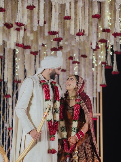 A stolen glance between the couple, framed by the beautiful ivory and red floral mandap. These are the unscripted moments of connection that we love to create the space for.