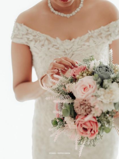 A close-up on the bride's hands gently touching her beautiful pastel bouquet, highlighting the intricate details of both.