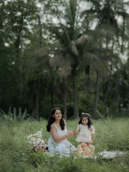 A mother and daughter sit in a grassy field surrounded by palm trees, enjoying a picnic. This is not just a family photo, but a chapter of life, capturing the simple joys of an outdoor family shoot.