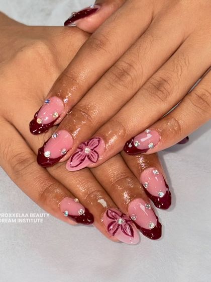 Tiny canvases, major flex. This bold set features a deep burgundy French tip, sparkling rhinestones, and a hand-painted floral accent nail.