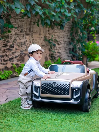 This little boy is ready to go for a drive in his luxury toy car. The green grass and natural stone wall provide a lovely backdrop for this outdoor portrait.