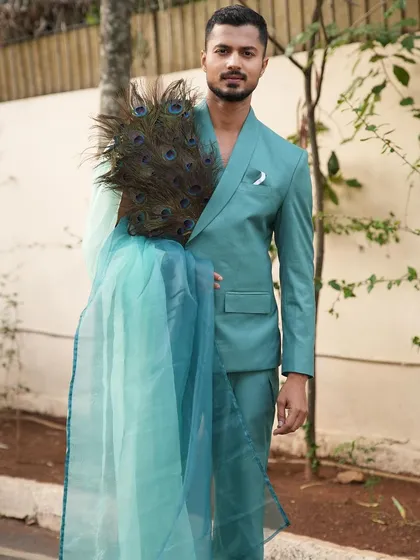 A direct-to-camera shot in a teal wrap-style suit, holding peacock feathers as a prop to enhance the artistic vision.