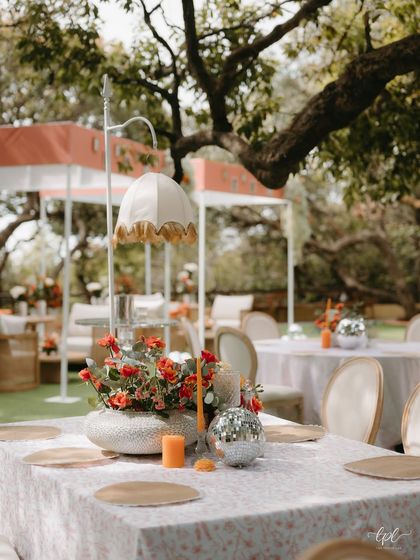 A unique table centerpiece featuring a vintage-style lamp, orange florals, and a small disco ball.