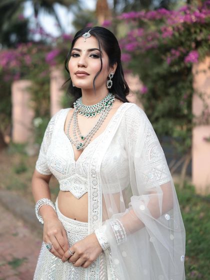 A three-quarter view of the white lehenga and layered diamond necklace, highlighting the intricate embroidery on the outfit.