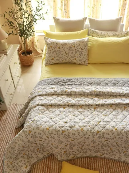 Your bedroom should be your sanctuary. We create complete bedding sets, from soft cotton bedsheets to beautifully printed quilts and matching pillow covers. This cozy setup features our 'Winged Skies' quilt, designed to bring cheerful, sunny vibes to your space.