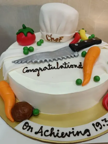 A "Congratulations" cake for a new chef. The design features a chef's hat, a knife, and various fondant vegetables.